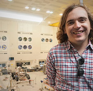 Thomas Connor with Mars Rover in background in a large, white room