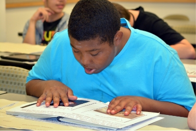 Photo of an African American boy reading a braille book of astronomy.